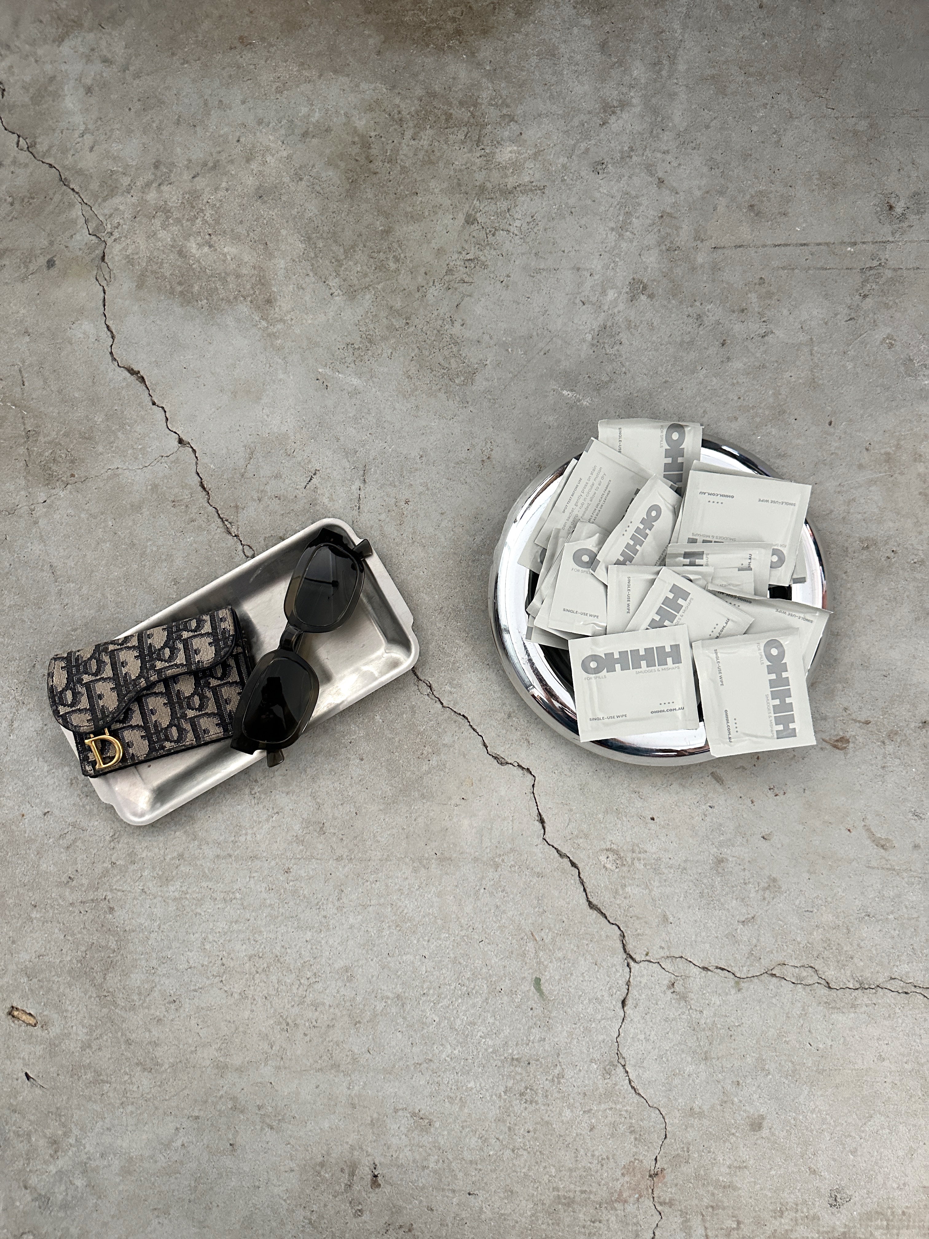 OHHH individual stain remover wipe sachets styled with sunglasses and wallet, on-the-go stain wipes